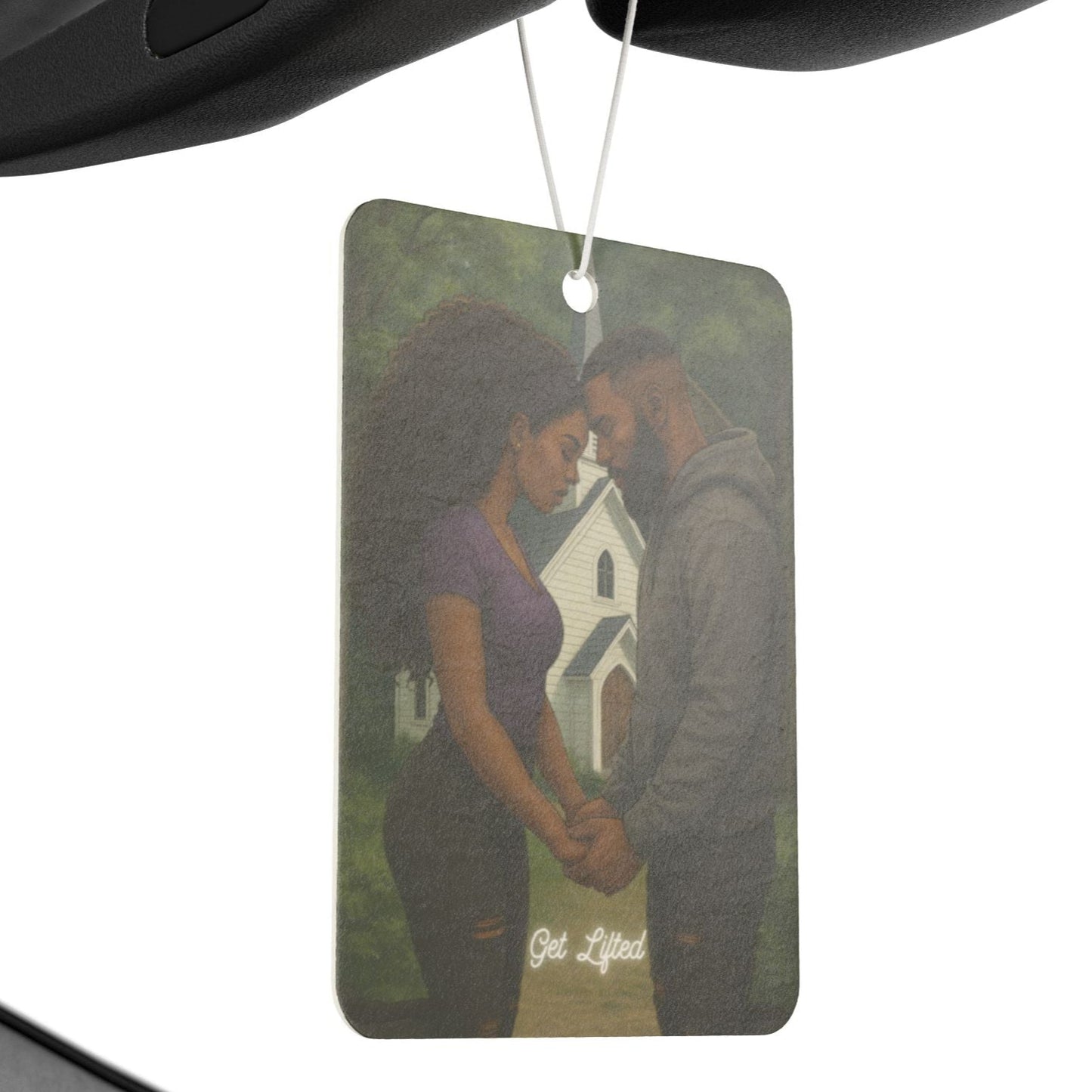 Air freshener with a couple holding hands in front of a house hanging from a car's rearview mirror.