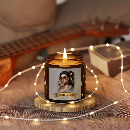 Candle with a label featuring a woman's face, surrounded by string lights on a textured surface with a guitar in the background.